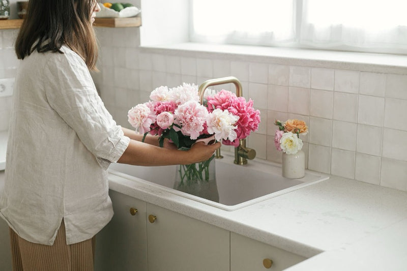 A person washing flowers next to a granite countertop.