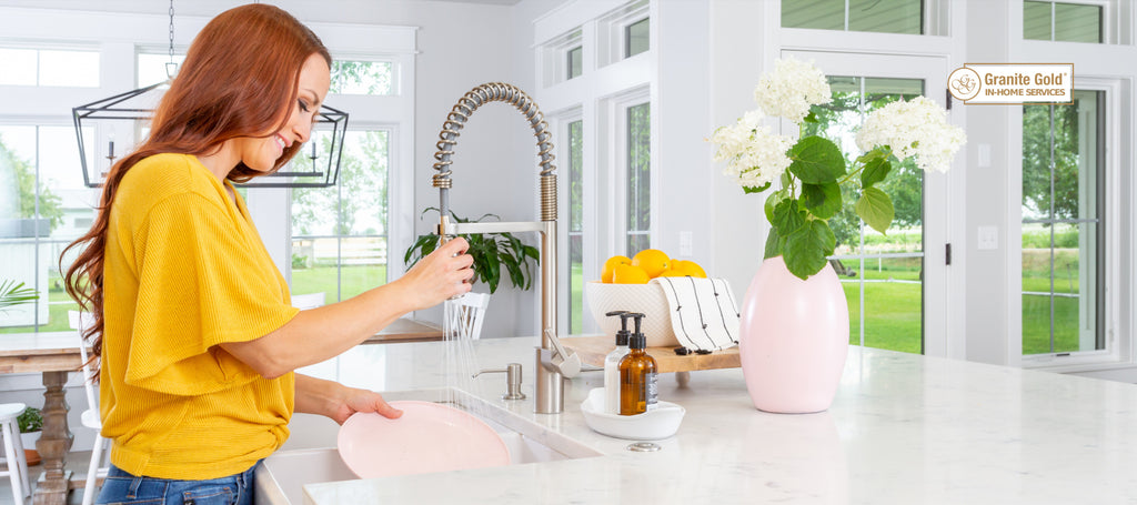 Woman washing dishes in her kitchen with white countertops 